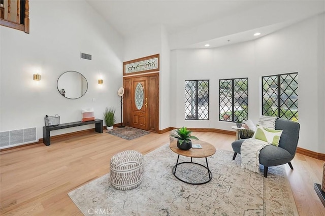 entrance foyer with baseboards, visible vents, wood finished floors, and high vaulted ceiling