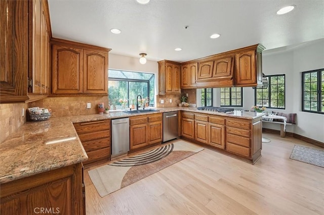 kitchen featuring brown cabinetry, light wood-style floors, appliances with stainless steel finishes, a sink, and a peninsula