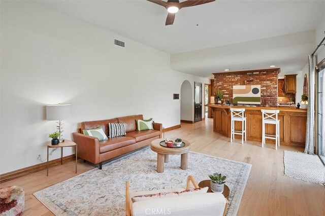 living area with light wood finished floors, a ceiling fan, visible vents, baseboards, and arched walkways