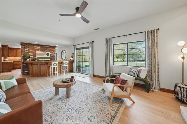 living room with baseboards, visible vents, ceiling fan, and light wood-style floors