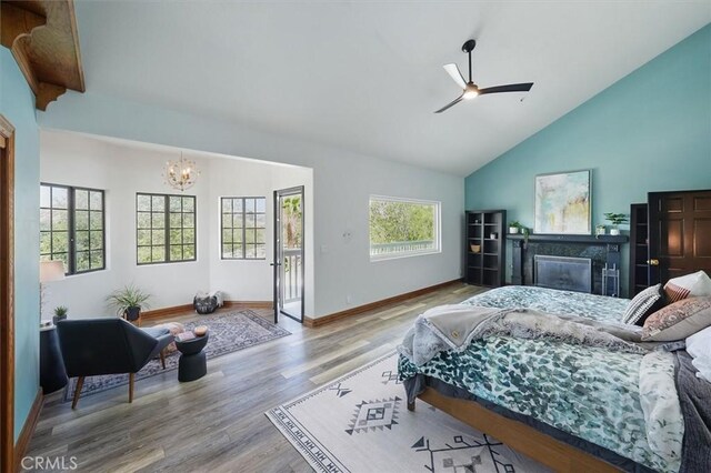 bedroom with a tile fireplace, high vaulted ceiling, baseboards, wood finished floors, and ceiling fan with notable chandelier