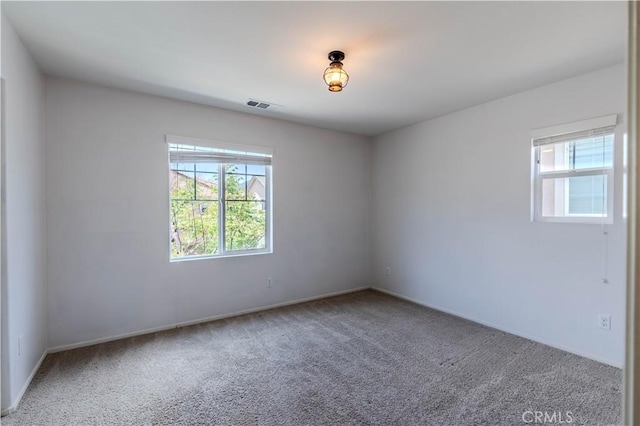 carpeted empty room featuring visible vents, a healthy amount of sunlight, and baseboards