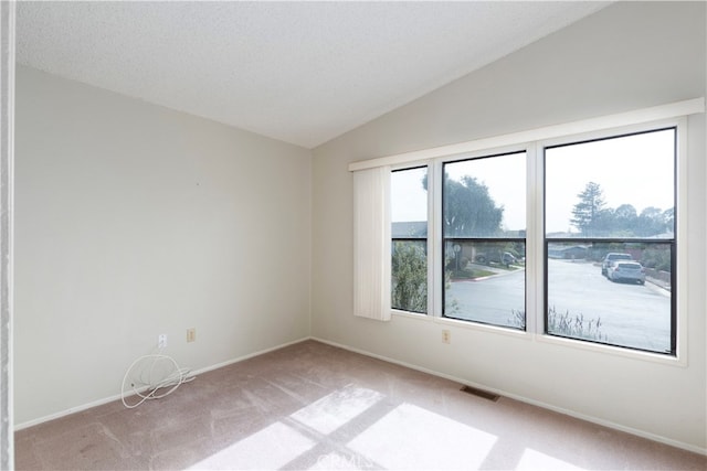 empty room featuring visible vents, vaulted ceiling, light colored carpet, and baseboards