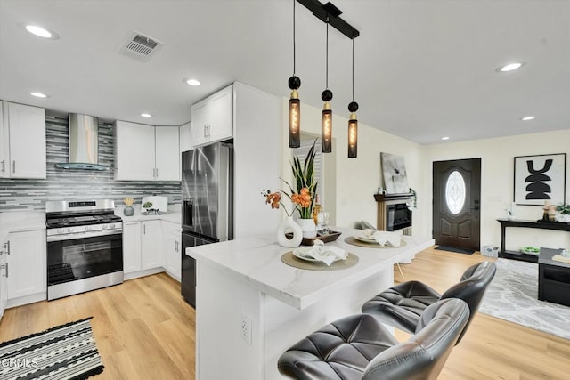 17632 E Covina Blvd, Covina, CA 91722 - kitchen featuring stainless steel appliances, wall chimney range hood, a kitchen bar, light wood-type flooring, and white cabinetry