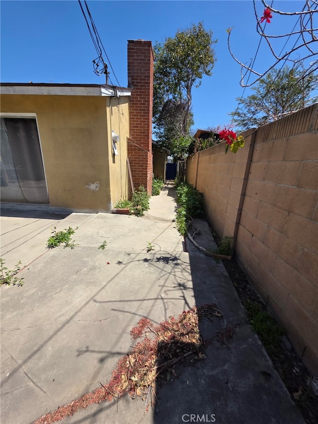 view of property exterior with a chimney, fence, stucco siding, and a patio area