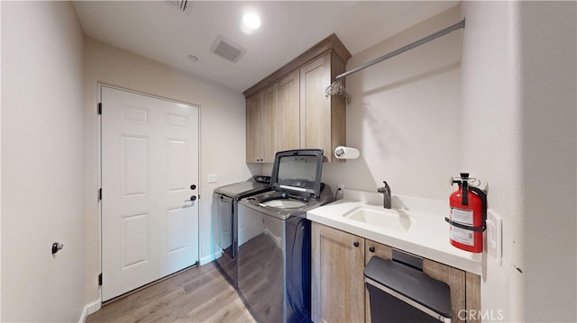 laundry area with a sink, cabinet space, washing machine and clothes dryer, visible vents, and light wood-style flooring