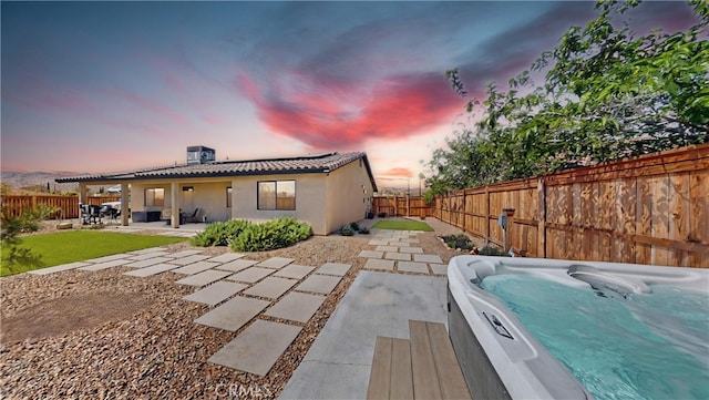 back of house with a tiled roof, a patio area, a fenced backyard, and a hot tub