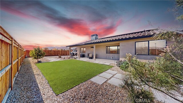 back of house at dusk with a patio, a yard, a fenced backyard, a tiled roof, and stucco siding