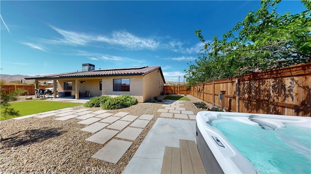 view of side of home featuring stucco siding, a patio area, a fenced backyard, and a hot tub
