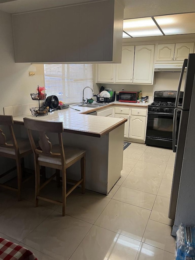 kitchen with a sink, a peninsula, freestanding refrigerator, black range with gas stovetop, and a kitchen bar