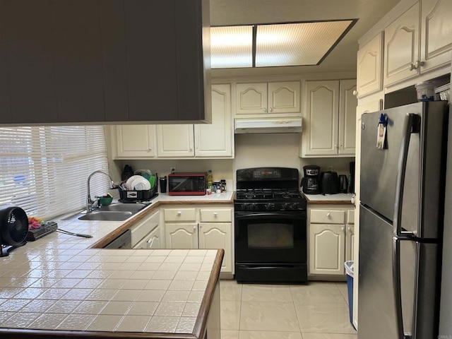 kitchen featuring a sink, freestanding refrigerator, tile countertops, and black gas stove