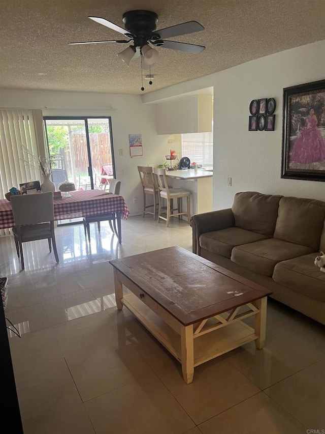 living area featuring a textured ceiling, light tile patterned flooring, and ceiling fan