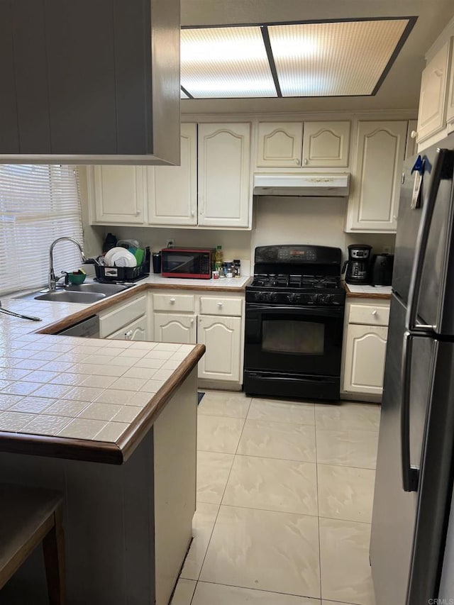 kitchen with a sink, freestanding refrigerator, black range with gas stovetop, under cabinet range hood, and tile counters