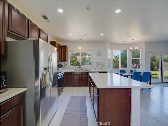 kitchen with decorative backsplash, appliances with stainless steel finishes, a kitchen island, a sink, and visible vents