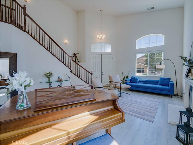 living area with visible vents, stairway, an inviting chandelier, and a high ceiling