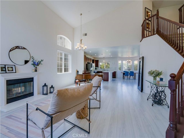living room with light wood finished floors, a notable chandelier, high vaulted ceiling, stairs, and visible vents