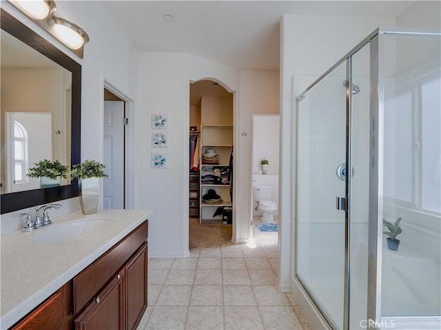 bathroom featuring toilet, a walk in closet, a shower stall, and vanity