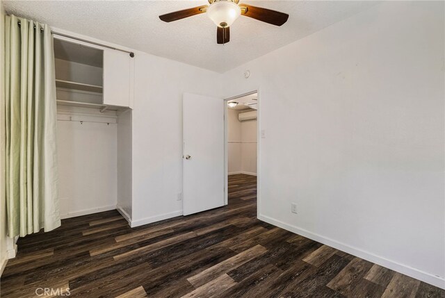 unfurnished bedroom with ceiling fan, baseboards, a closet, an AC wall unit, and dark wood-type flooring