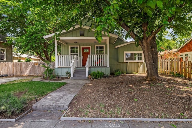 bungalow-style house with a porch, board and batten siding, and fence