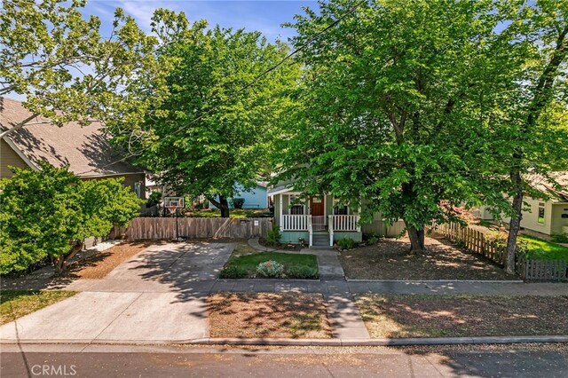 view of property hidden behind natural elements featuring a porch and fence private yard