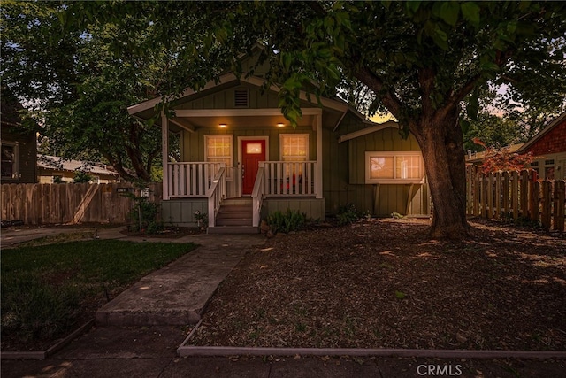 bungalow-style house with a porch, fence, and board and batten siding