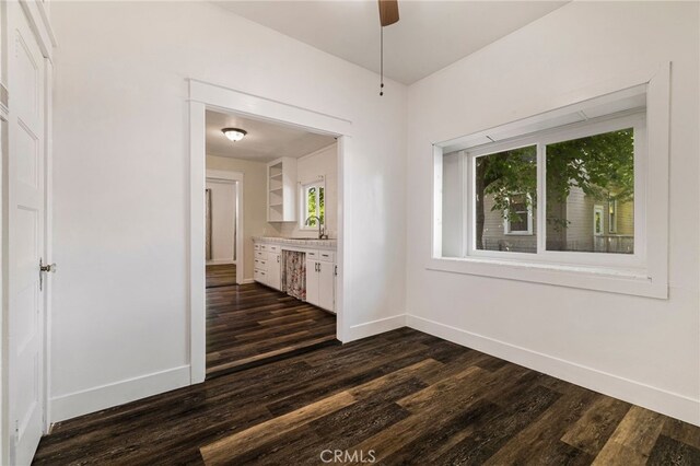 empty room with dark wood-style flooring, baseboards, ceiling fan, and a sink