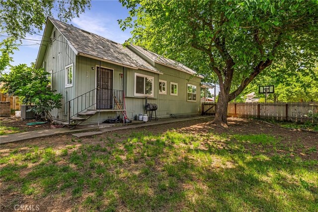 bungalow-style home featuring central air condition unit, a fenced backyard, and roof with shingles