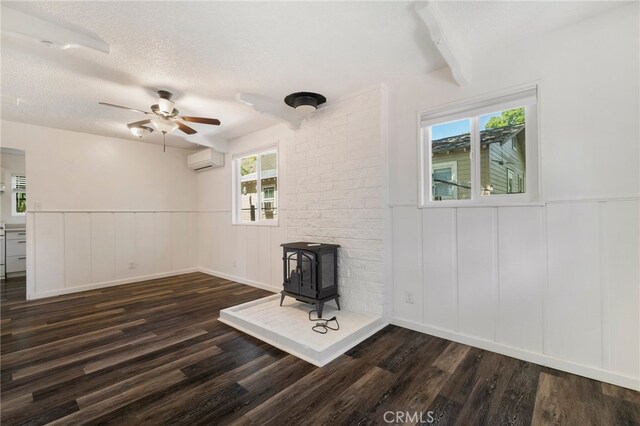 spare room featuring a ceiling fan, dark wood-style flooring, a wood stove, an AC wall unit, and a decorative wall