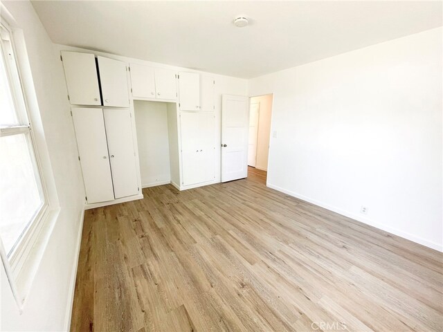 unfurnished bedroom with a closet, light wood-style flooring, and baseboards