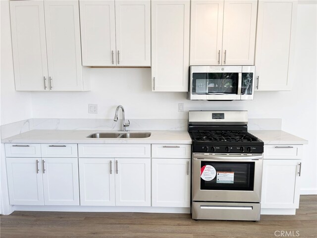 kitchen featuring white cabinets, a sink, stainless steel appliances, light stone countertops, and wood finished floors