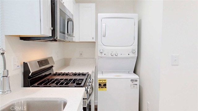 kitchen featuring white cabinetry, stacked washer / dryer, a sink, stainless steel appliances, and light stone countertops