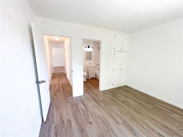 unfurnished bedroom with baseboards, light wood-type flooring, and ensuite bath