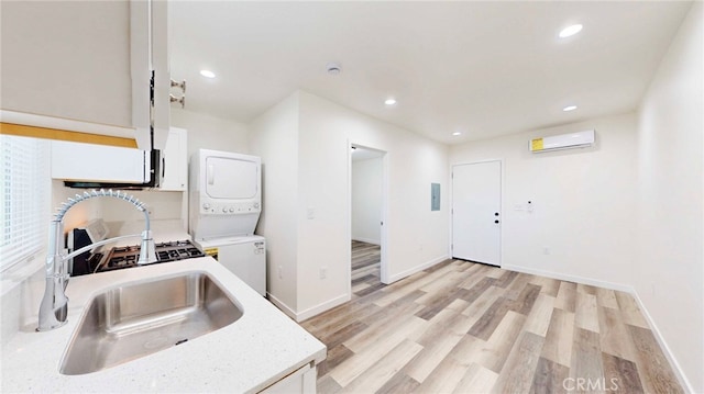 kitchen featuring white cabinetry, a sink, stacked washer and clothes dryer, light wood finished floors, and a wall mounted air conditioner
