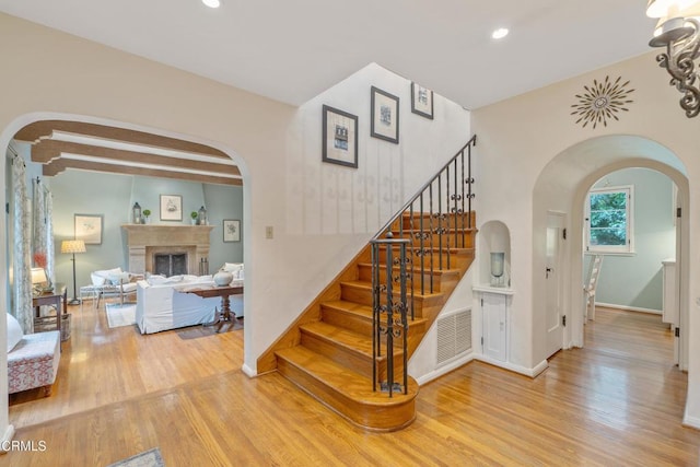 stairway with recessed lighting, a fireplace, baseboards, arched walkways, and wood finished floors