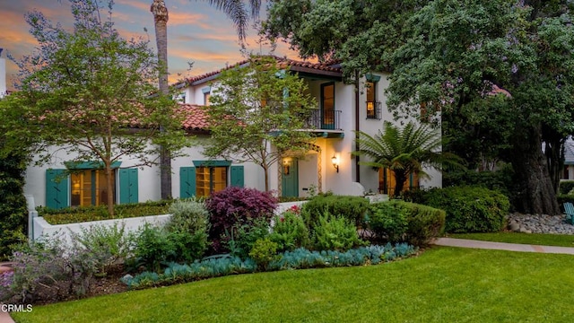 view of front of house with a front yard, stucco siding, a tiled roof, and a balcony