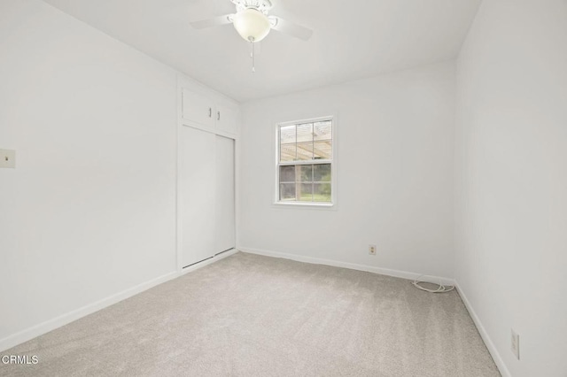 spare room featuring light colored carpet, a ceiling fan, and baseboards