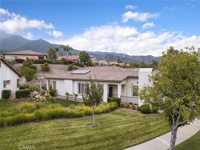 mediterranean / spanish-style house featuring a tile roof, a front yard, a mountain view, solar panels, and stucco siding