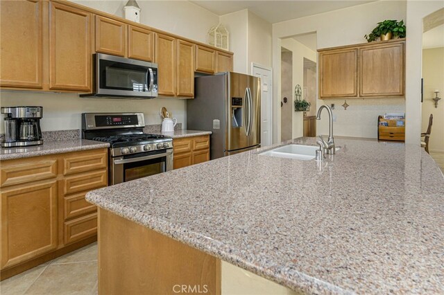 kitchen featuring light stone counters, a sink, stainless steel appliances, light tile patterned flooring, and an island with sink