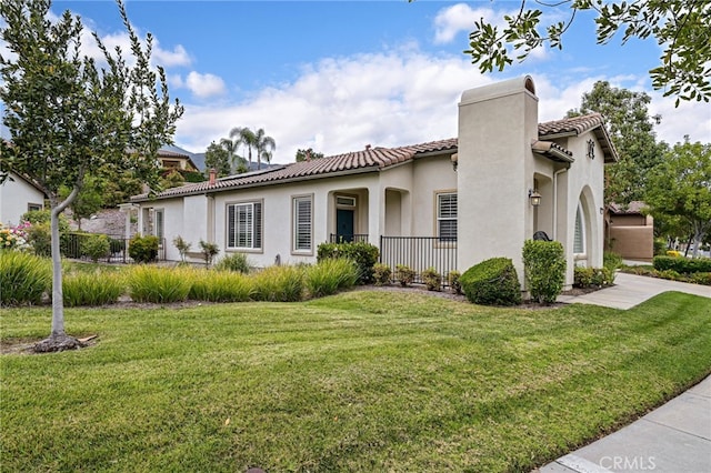 mediterranean / spanish-style home featuring a chimney, a front lawn, a tile roof, and stucco siding