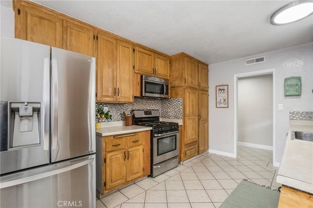 kitchen featuring light tile patterned floors, appliances with stainless steel finishes, light countertops, brown cabinetry, and backsplash