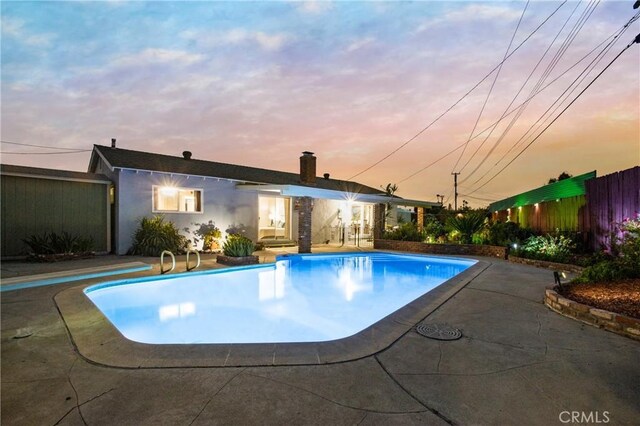 pool at dusk with fence, an outdoor pool, and a patio
