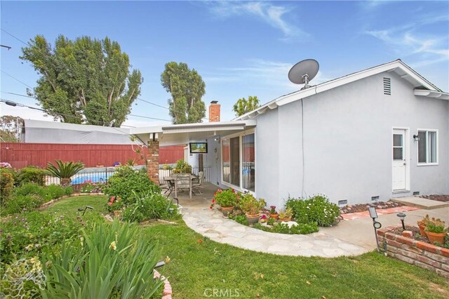 rear view of property featuring a patio, a lawn, a chimney, stucco siding, and fence