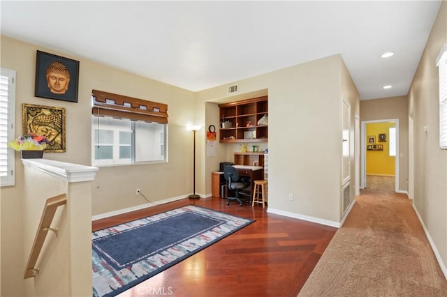 office area with built in desk, visible vents, wood finished floors, and baseboards