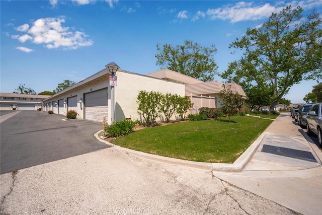 view of side of home featuring stucco siding, a yard, and community garages