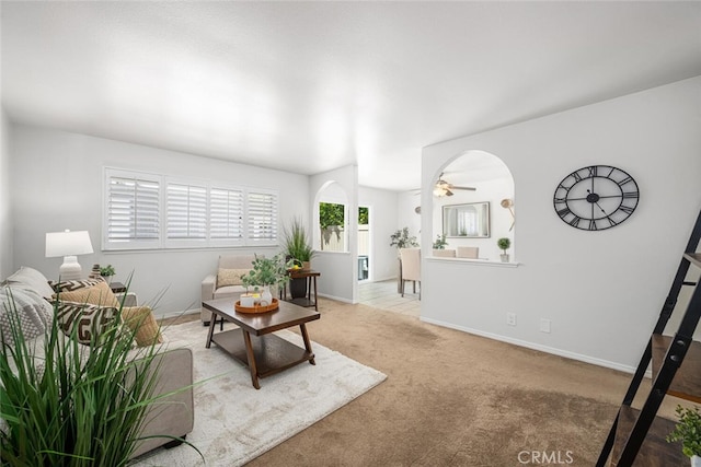carpeted living area featuring baseboards, arched walkways, and ceiling fan