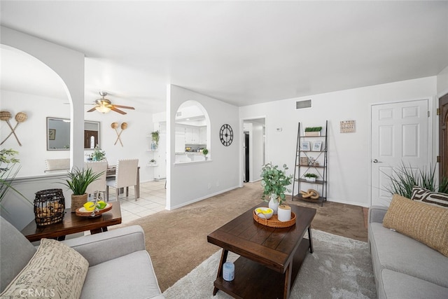 living area with light colored carpet, a ceiling fan, visible vents, and arched walkways