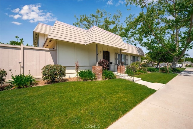 view of front of house with fence, stucco siding, and a front lawn