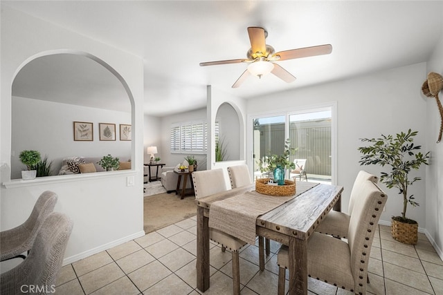 dining area featuring light tile patterned floors, arched walkways, baseboards, and a ceiling fan