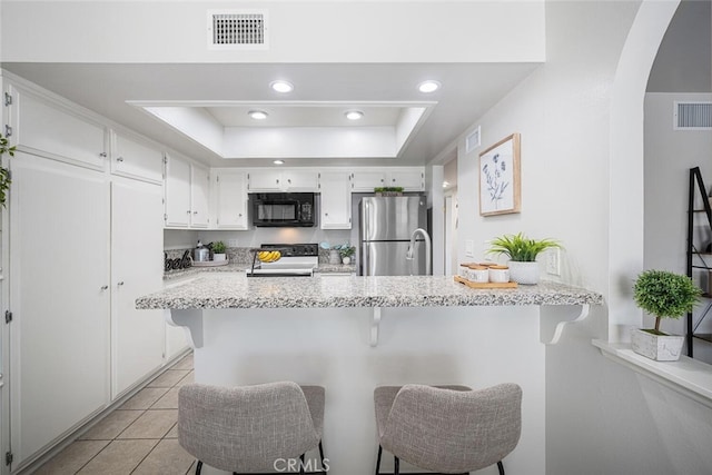 kitchen featuring black microwave, arched walkways, range, freestanding refrigerator, and visible vents