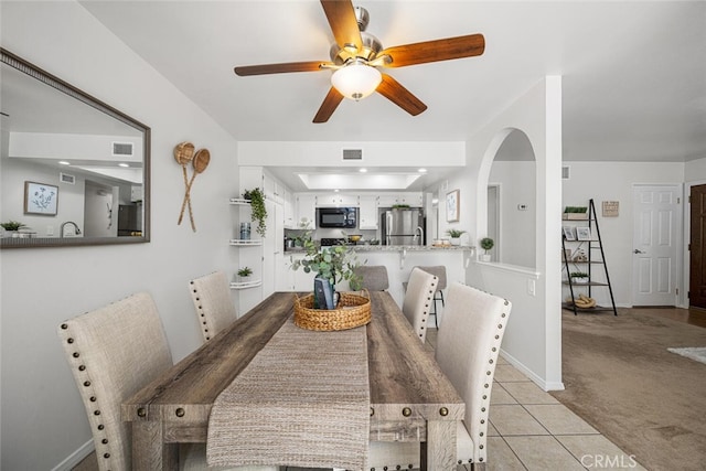 dining space featuring visible vents, light carpet, ceiling fan, arched walkways, and light tile patterned floors